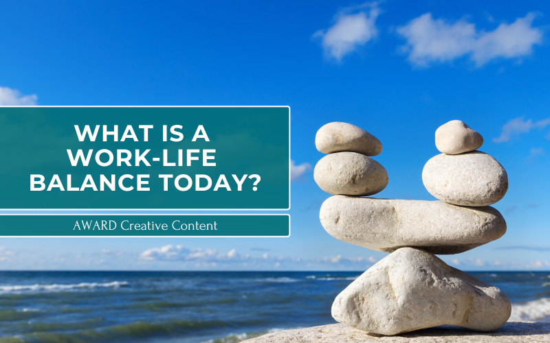 Balanced stones by the ocean under a clear sky with text reading 'What is a Work Life Balance Today?' by AWARD Creative Content.